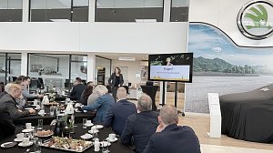Eine Rednerin steht im �koda-Ausstellungsraum vor einem Bildschirm mit der Folie Fragen? Vielen Dank f&uuml;r Ihre Aufmerksamkeit!. G&auml;ste sitzen an gedeckten Fr&uuml;hst&uuml;ckstischen und h&ouml;ren zu.