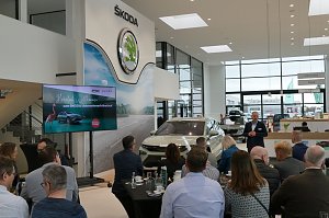 Viele G&auml;ste sitzen an Tischen im Showroom, w&auml;hrend ein Referent den neuen �koda Elroq pr&auml;sentiert. Links der Begr&uuml;&szlig;ungsbildschirm, rechts der Empfangsbereich des Autohauses.