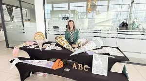 Eine Frau sitzt hinter einem Stand im Autohaus. Auf den Tischen liegen farbenfrohe, gro&szlig;e Schult&uuml;ten und Informationsmaterialien. Vorne gro&szlig;e Buchstaben ABC.