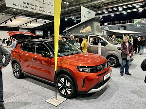Ein roter Opel SUV im Vordergrund, dahinter ein Opel Crosscamp Camper mit ge&ouml;ffnetem Hochdach. Besucher stehen daneben.