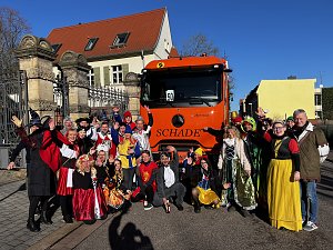 "Gruppe von kost&uuml;mierten Menschen in M&auml;rchen- und Tierverkleidungen posiert vor einem orangefarbenen LKW mit der Aufschrift �SCHADE�.