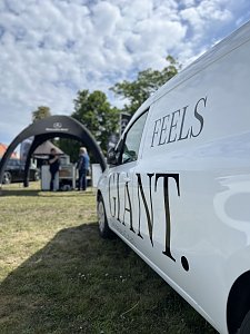 Wei&szlig;er Transporter mit Schriftzug: Seitliche Nahaufnahme eines wei&szlig;en Fahrzeugs mit dem Schriftzug Feels Giant auf der Messefl&auml;che.