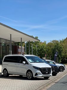 Ein wei&szlig;er Mercedes-Benz Van ist vor der Stadthalle Wittenberg geparkt, dahinter ein weiteres schwarzes Fahrzeug und eine Mercedes-Fahne.