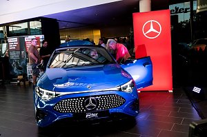 Ein blauer Mercedes CLA wird im Showroom pr&auml;sentiert. Mehrere Besucher betrachten das Auto, w&auml;hrend ein Mann in den Innenraum schaut.