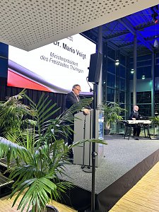 Redner am Pult auf der B&uuml;hne der Automobil Messe Erfurt, Leinwand: Dr. Mario Voigt, Ministerpr&auml;sident Th&uuml;ringen, rechts ein Keyboardspieler.