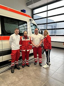 Vier Personen in DRK-Dienstkleidung stehen in einer Halle vor einem Rettungswagen.