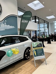 Wei&szlig;er Skoda im Autohaus mit Ballons, daneben Aufsteller Gewinnspiel und Skoda-Peter-Beachflag im Hintergrund.