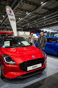 Roter Suzuki auf der Automesse, zwei Besucher begutachten das Fahrzeug.