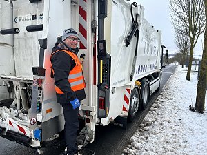 Verkaufsberater vom Autohaus Peter Andr&eacute; Schmidt steht auf der Trittstufe eines M&uuml;llfahrzeugs w&auml;hrend der Fahrt durch ein Industriegebiet.