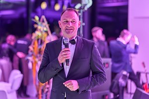 Mann im Anzug mit Mikrofon bei Gala-Event mit lila Beleuchtung.