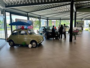 2 Fiats mit Luftballons im Showroom vor einer bunten "La Dolce Vita"-Wand, mehrere Personen daneben.




