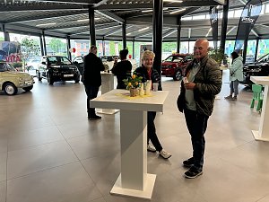 Mehrere Personen im Autohaus Showroom an Stehtischen, im Hintergrund Fahrzeuge der Marke Fiat


