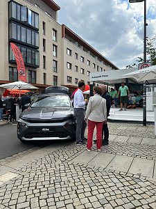 �koda Roadshow B&uuml;hne im Hintergrund; davor graues Skoda Fahrzeug mit mehreren interessierten Personen daneben.



