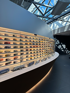 Eine riesige, geschwungene Vitrinenwand pr&auml;sentiert unz&auml;hlige Lkw-Modelle im Miniaturformat auf beleuchteten Regalb&ouml;den.