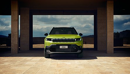 Der neue Jeep&reg; Compass e-Hybrid - Gr&uuml;ner Jeep Compass von vorne, steht auf einer Terrasse vor einer modernen Steinmauer mit Berglandschaft im Hintergrund.