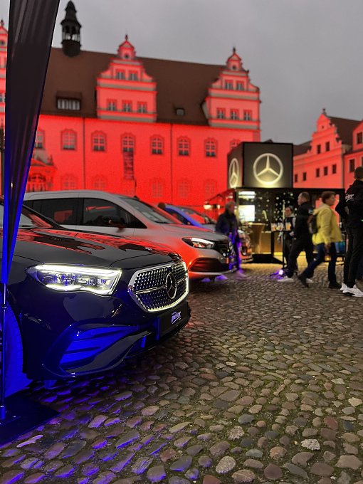 Im Vordergrund zu sehen ist eine Auswahl der aktuellen Mercedes-Benz Modellen gekonnt in Szene gesetzt mit farbenfroher Beleuchtung in mitten der Wittenberger Altstadt. 